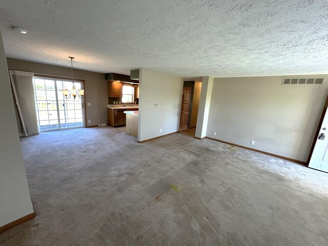 unfurnished living room with a chandelier, a textured ceiling, baseboards, and light colored carpet
