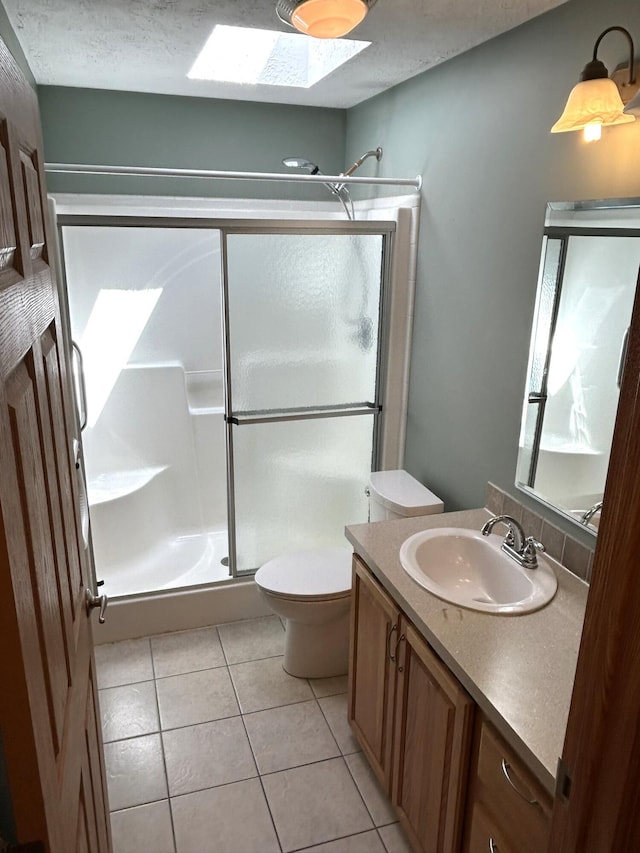 full bath featuring a skylight, a shower stall, tile patterned floors, vanity, and a textured ceiling