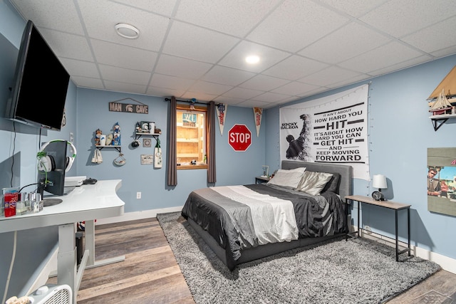 bedroom with a paneled ceiling, baseboards, and wood finished floors