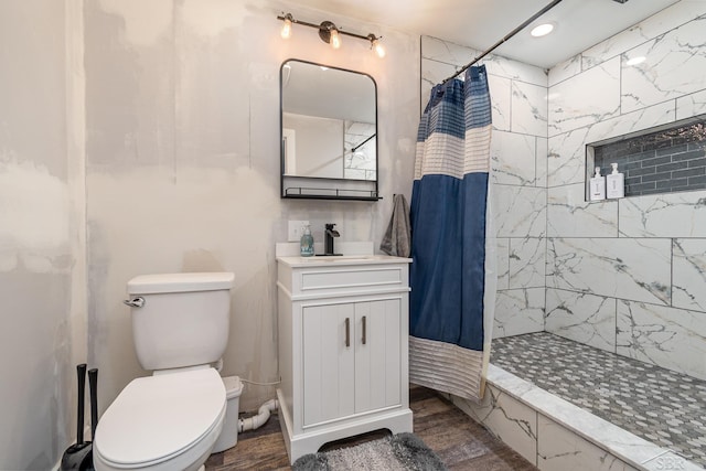 bathroom featuring a tile shower, vanity, toilet, and wood finished floors