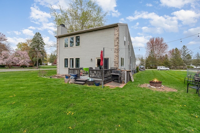 back of property featuring an outdoor fire pit, a chimney, a lawn, and a deck