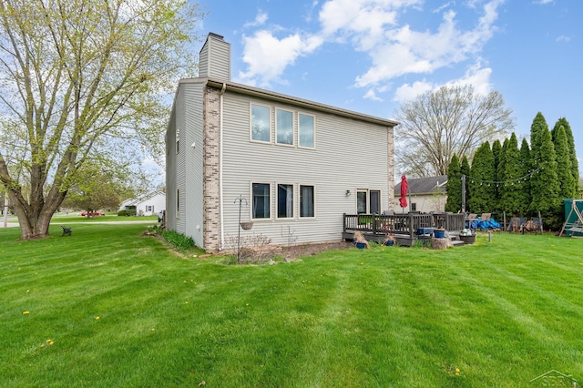rear view of house with a chimney, a deck, and a lawn