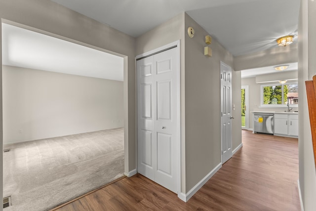 hall featuring wood finished floors, a sink, and baseboards