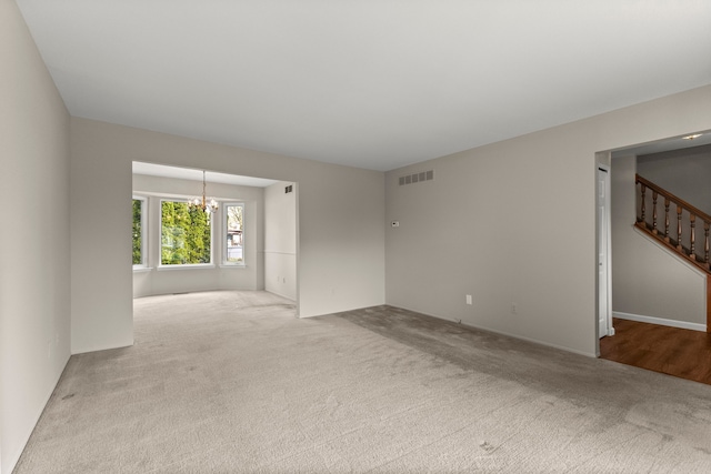 spare room featuring a chandelier, carpet flooring, and stairway
