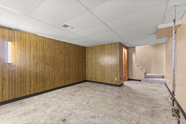 finished below grade area featuring a paneled ceiling, wood walls, and baseboards