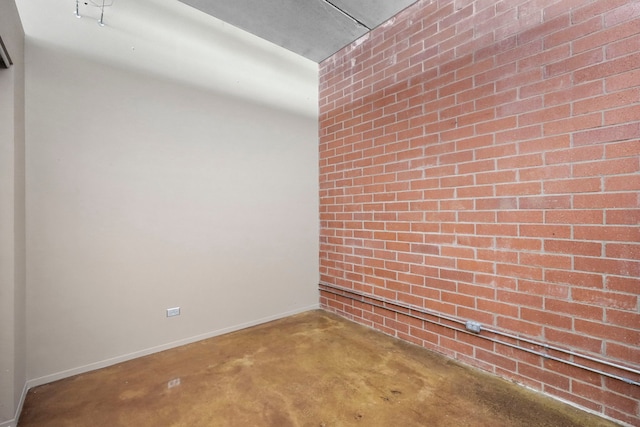 empty room with concrete floors, baseboards, and brick wall