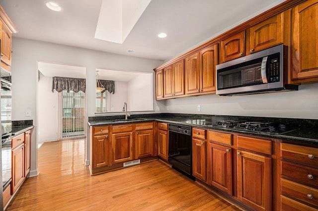 kitchen featuring black appliances, a sink, a skylight, light wood-style flooring, and recessed lighting