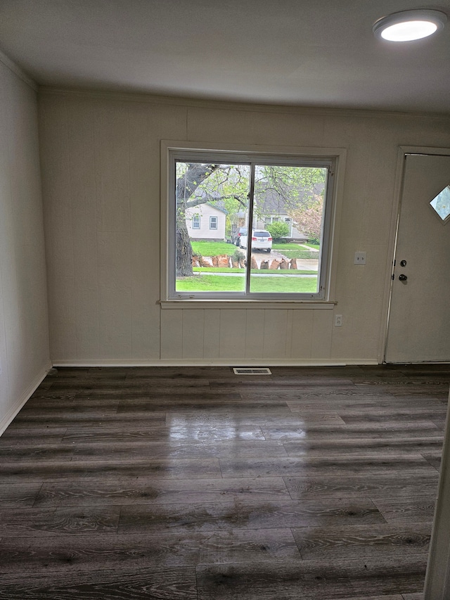 empty room with a healthy amount of sunlight, dark wood-style flooring, and visible vents
