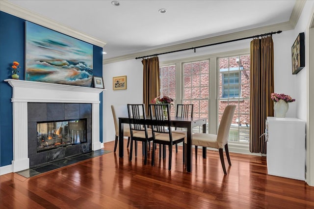 dining area with ornamental molding, wood finished floors, a tiled fireplace, and recessed lighting