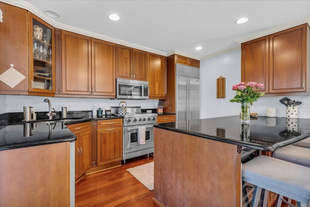 kitchen with high quality appliances, a sink, a kitchen breakfast bar, wood finished floors, and glass insert cabinets