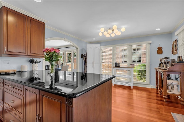 kitchen featuring arched walkways, ornamental molding, light wood finished floors, recessed lighting, and brown cabinets