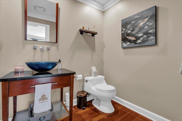 half bath featuring crown molding, wood finished floors, baseboards, toilet, and vanity