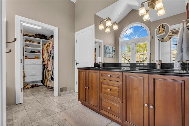 full bathroom featuring high vaulted ceiling, double vanity, a walk in closet, and a chandelier