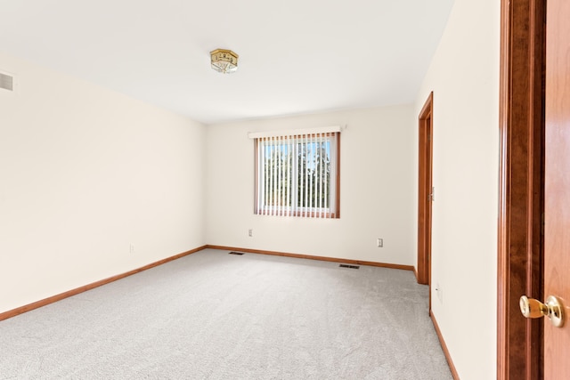 spare room featuring light colored carpet, visible vents, and baseboards