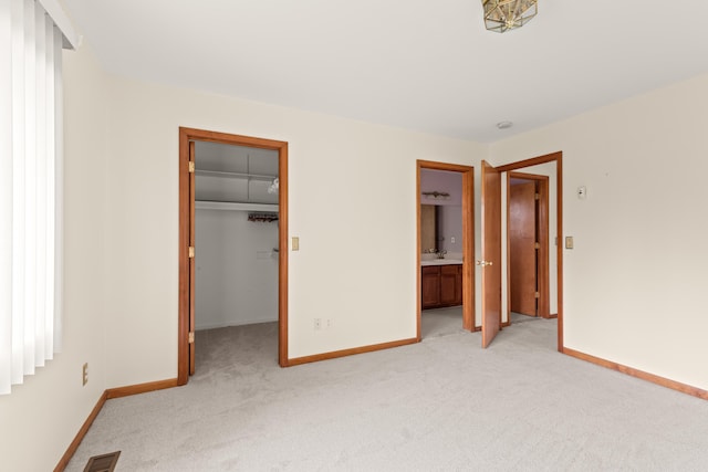 unfurnished bedroom with baseboards, a spacious closet, light carpet, and visible vents