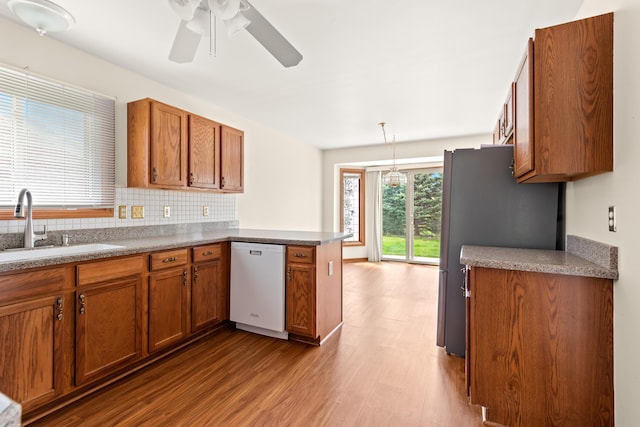 kitchen with a sink, a peninsula, brown cabinetry, and dishwasher