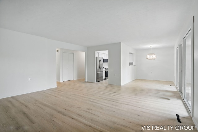 unfurnished living room with baseboards, an inviting chandelier, and light wood-type flooring