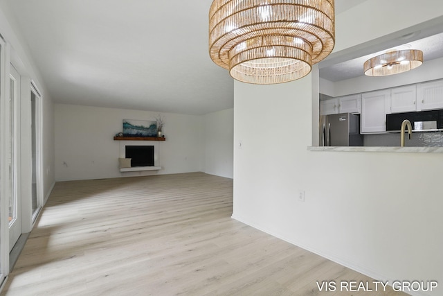unfurnished living room with light wood-type flooring, a fireplace, and a notable chandelier