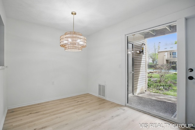 unfurnished dining area with a notable chandelier, baseboards, visible vents, and wood finished floors