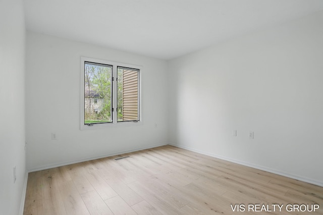 spare room with light wood finished floors, visible vents, and baseboards