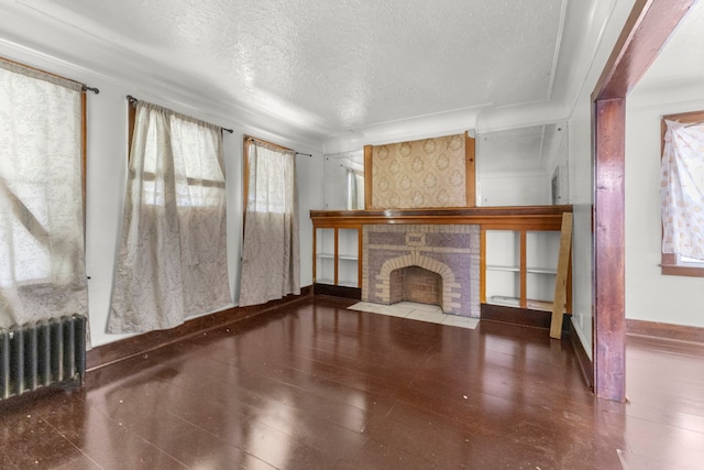 unfurnished living room with baseboards, radiator, a fireplace, and a textured ceiling