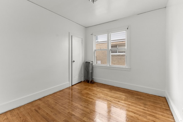 empty room with radiator, light wood-type flooring, and baseboards