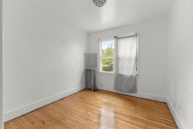 empty room with baseboards, radiator, and wood finished floors