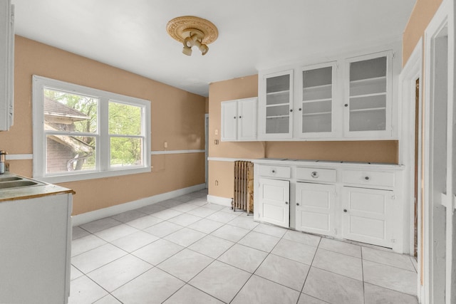 kitchen with light tile patterned floors, glass insert cabinets, white cabinets, baseboards, and light countertops