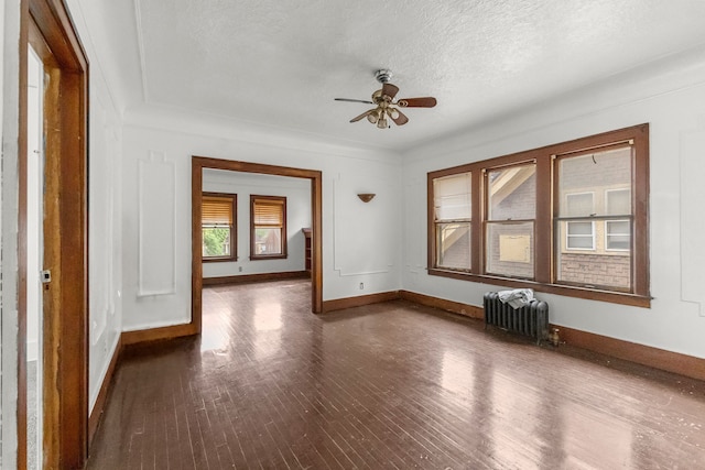 spare room featuring radiator, a textured ceiling, dark wood finished floors, a ceiling fan, and baseboards