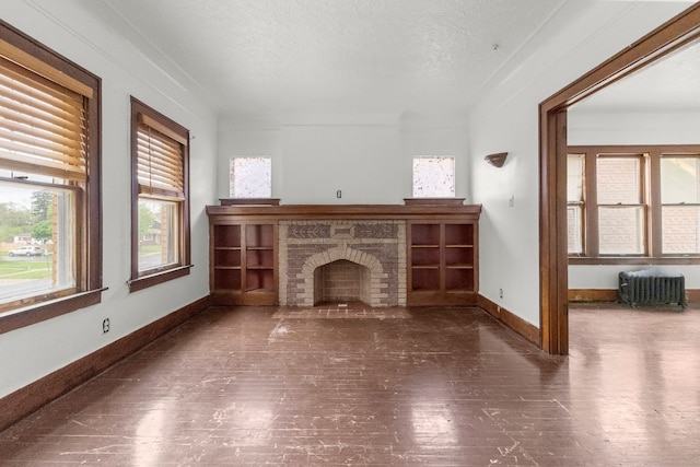 unfurnished living room featuring a textured ceiling, wood finished floors, baseboards, and a brick fireplace