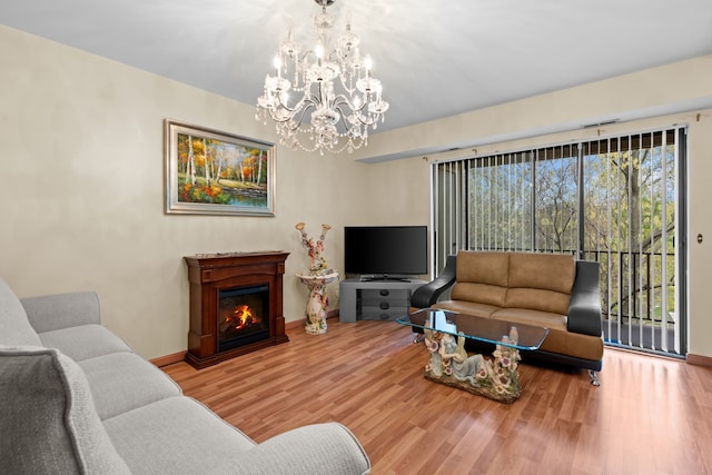 living room with a glass covered fireplace, baseboards, a chandelier, and wood finished floors