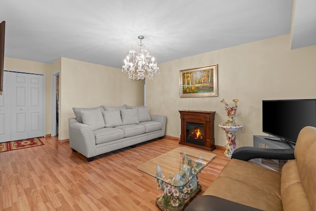 living area featuring an inviting chandelier, light wood-type flooring, a lit fireplace, and baseboards