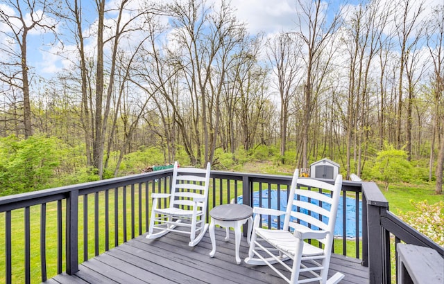 deck featuring a lawn, an outbuilding, a wooded view, and a storage unit
