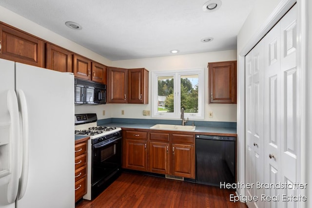 kitchen featuring brown cabinets, a sink, visible vents, dark wood-style flooring, and black appliances