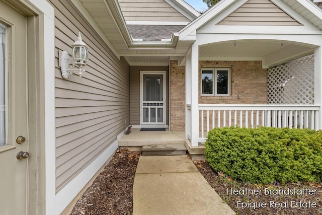 entrance to property with a porch, a shingled roof, and brick siding