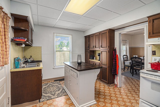 kitchen featuring electric range, a sink, under cabinet range hood, light flooring, and a drop ceiling