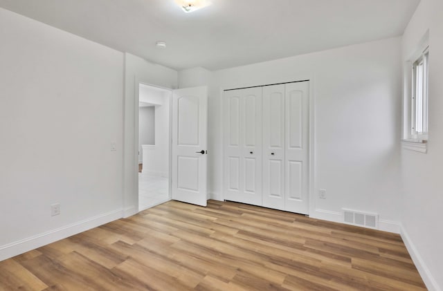 unfurnished bedroom featuring light wood-style floors, baseboards, and a closet