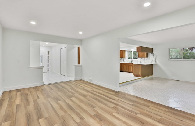 unfurnished living room featuring recessed lighting, a sink, baseboards, and light wood-style floors