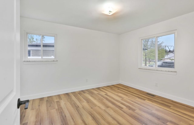 empty room with healthy amount of natural light, light wood-style flooring, and baseboards