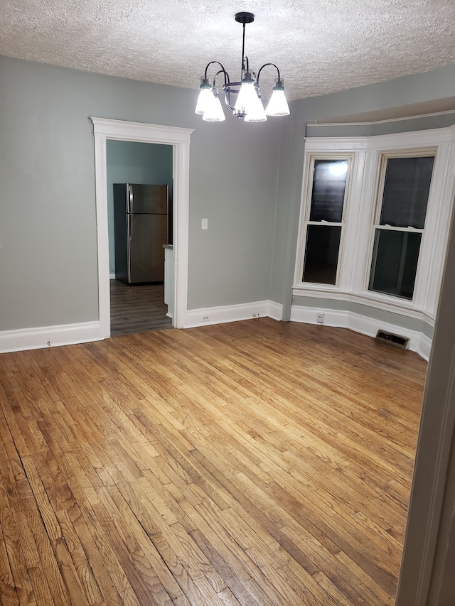 unfurnished dining area featuring a textured ceiling, visible vents, hardwood / wood-style floors, and a notable chandelier
