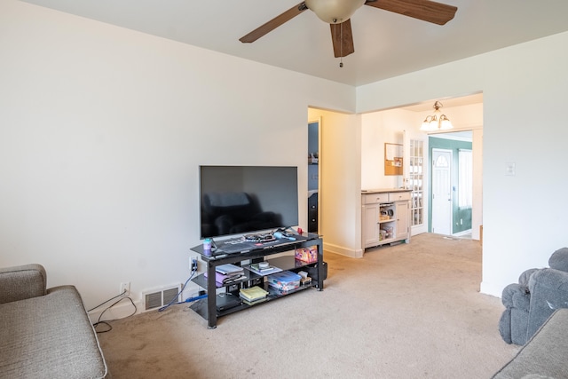 living room featuring light colored carpet, ceiling fan, baseboards, and a chandelier