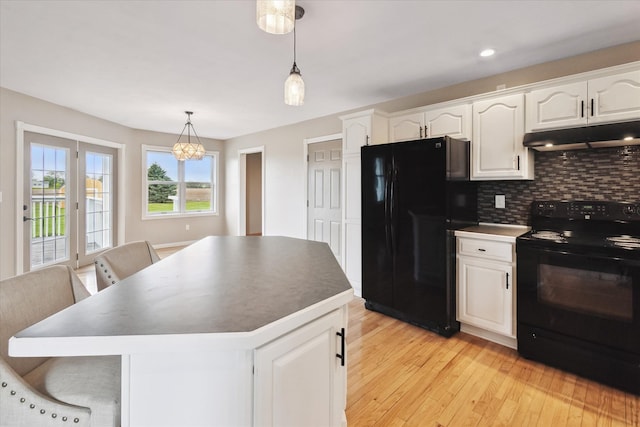 kitchen with under cabinet range hood, white cabinetry, black appliances, light wood-style floors, and tasteful backsplash