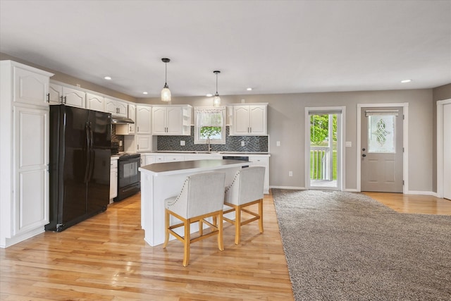 kitchen with a kitchen island, white cabinets, light wood-type flooring, black appliances, and decorative backsplash