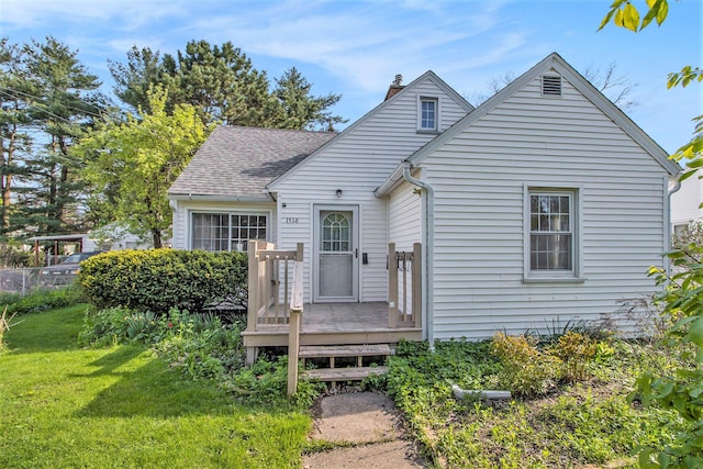 view of front of house with a chimney, a front yard, a wooden deck, and roof with shingles