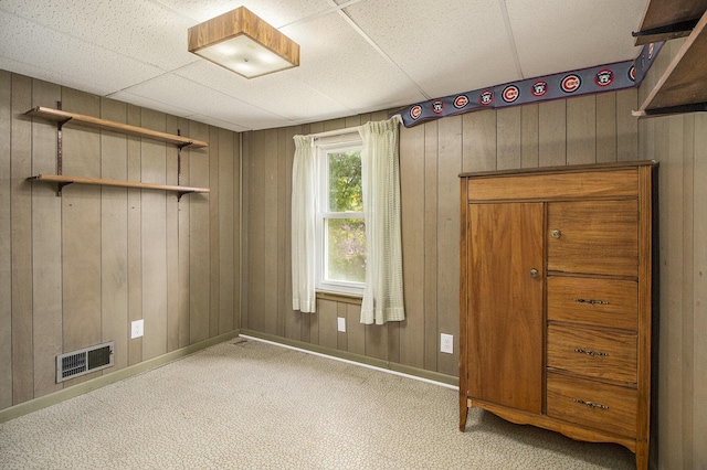 carpeted empty room with baseboards, wooden walls, and visible vents