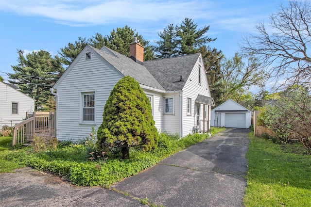 view of home's exterior featuring roof with shingles, a detached garage, aphalt driveway, an outbuilding, and a chimney