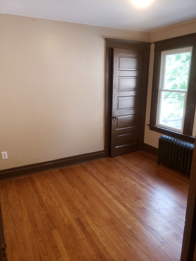 empty room with baseboards, radiator, and light wood finished floors