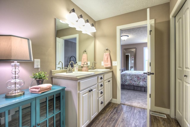 full bathroom with double vanity, wood finished floors, a sink, a textured ceiling, and visible vents