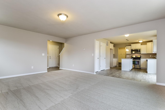 unfurnished living room featuring baseboards, light carpet, visible vents, and a sink