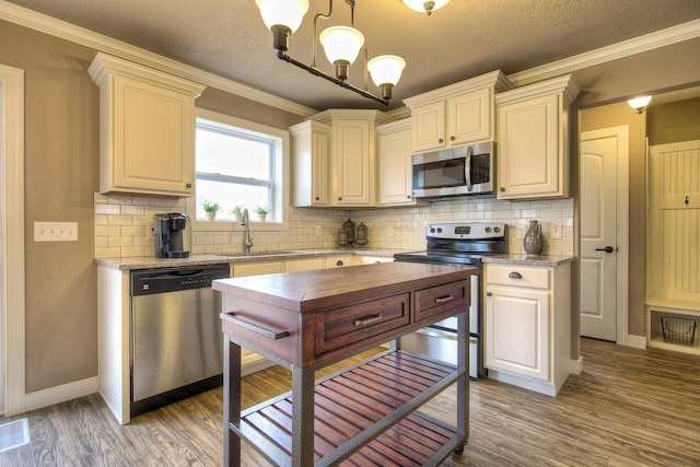 kitchen featuring ornamental molding, stainless steel appliances, a sink, and wood finished floors